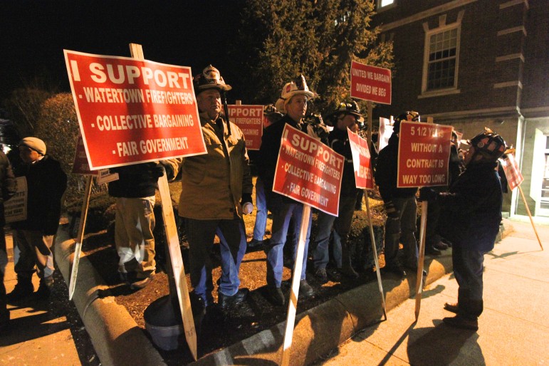 Firefighters hold signs outside Town Hall to request the fire contract be settled.