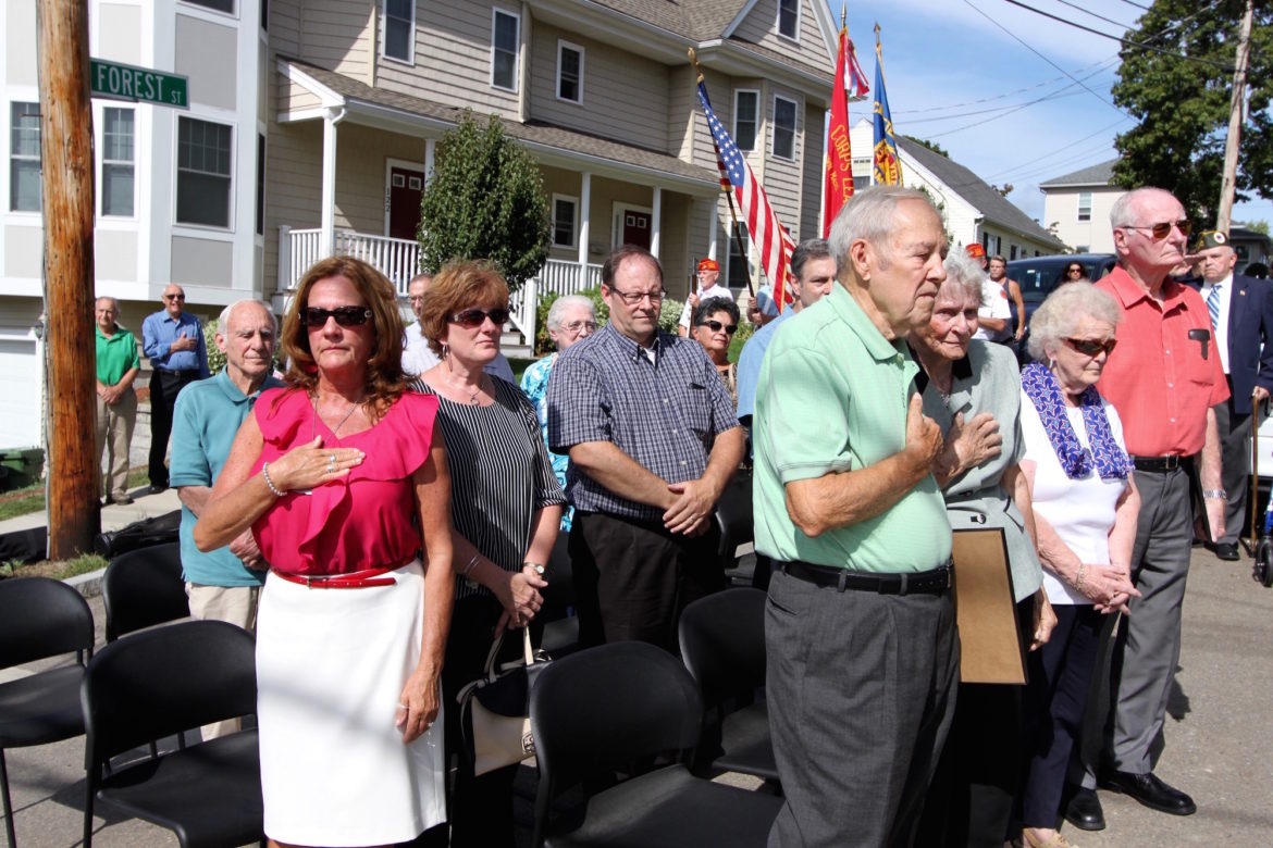 Attendees of the dedication of Dominic Joseph Russo Square rise while Taps is played. Among family members at the event were Russo's niece Mary, center, and his brother Dick, right.